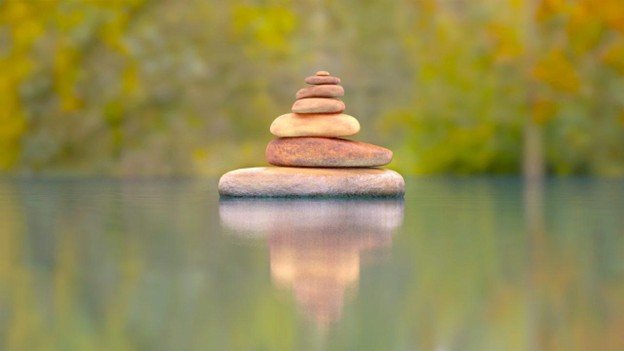 A cairn of balanced stones reflected in still water, a picture of steadiness amid changing surroundings