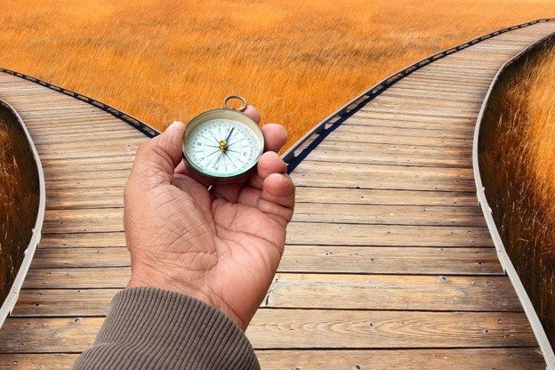 A hand holding a compass where a boardwalk path splits in two directions